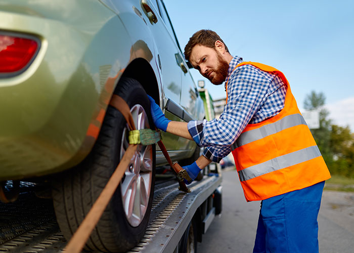 Man in an orange safety vest securing a car on a flatbed truck, illustrating people in the wrong place at the wrong time.