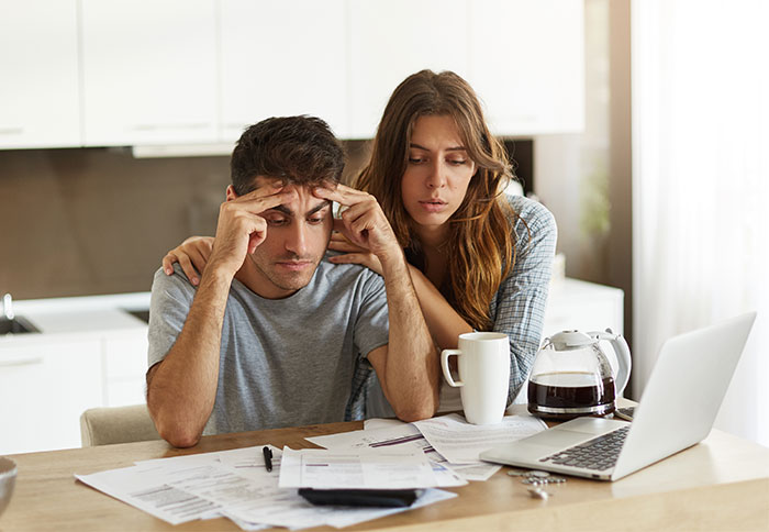 Stressed couple reviewing bills at home with wife comforting husband facing financial problems and divorce talks.
