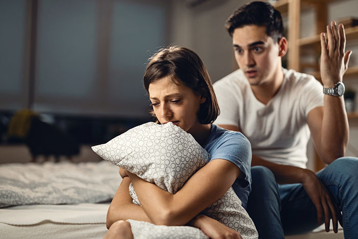 Sad mother clutching pillow looking distressed while husband argues, illustrating regrets becoming a parent.