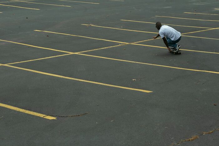 Man skateboarding alone in a large empty parking lot, highlighting unusual high school controversies and activities.