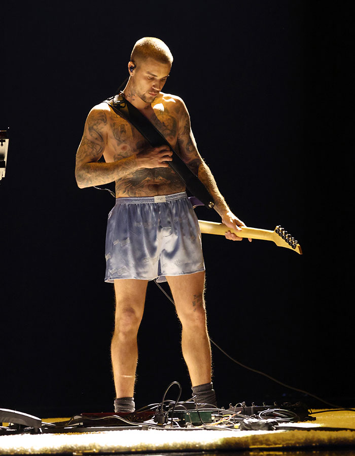 Tattooed musician shirtless playing electric guitar on stage wearing shorts during 2026 Grammy Awards cringe moments performance.