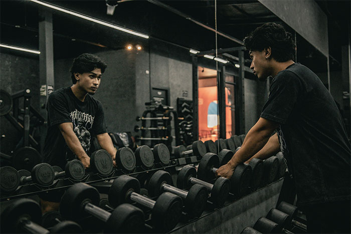 Young man lifting dumbbells at the gym with a focused expression, capturing the gym environment and equipment.