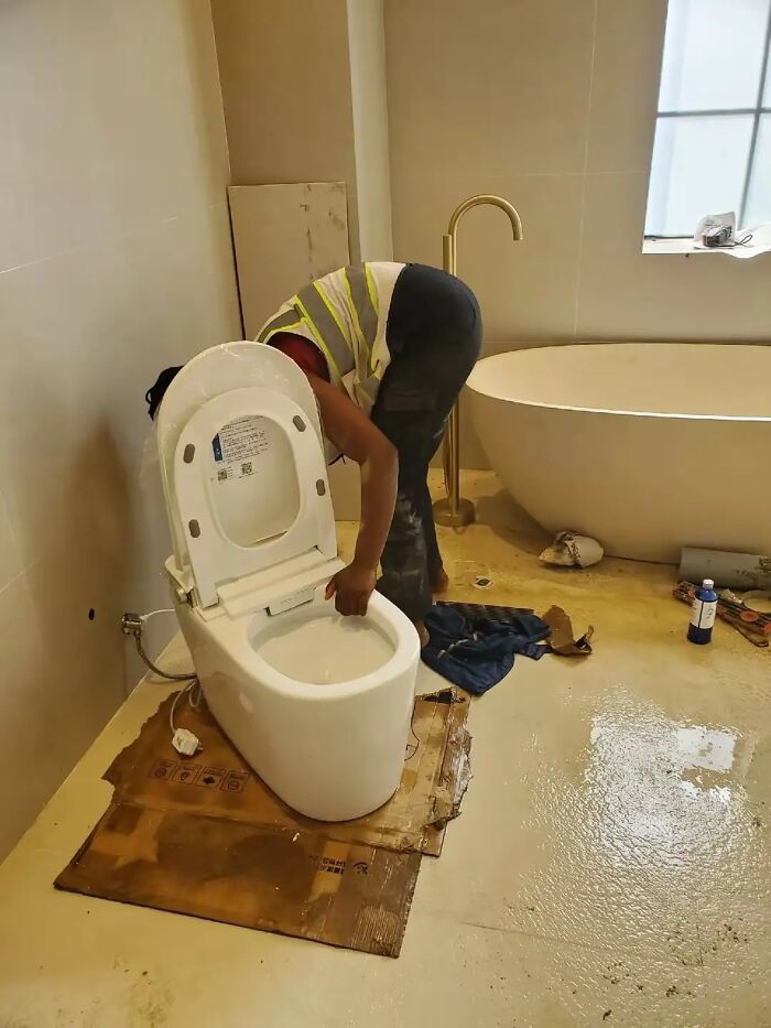 Worker in a high-visibility vest installing a modern toilet in a bathroom without nails done or painted nails visible.