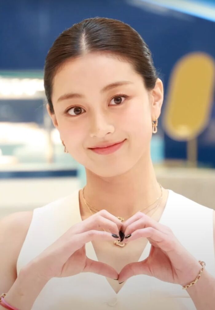 Jihyo smiling and forming a heart with her hands, showcasing her bio and career highlights in a bright setting.