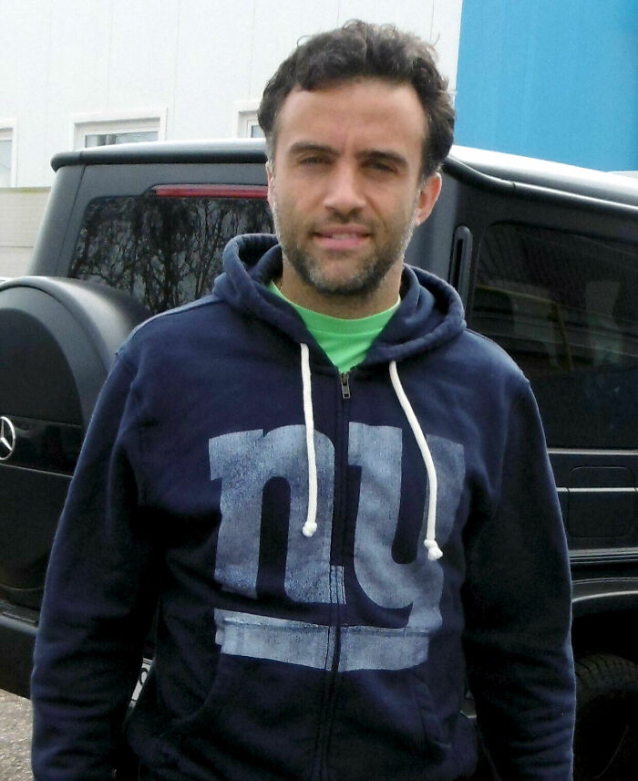 Giuseppe Rossi wearing a navy hoodie outdoors near a black vehicle, captured in a casual setting.