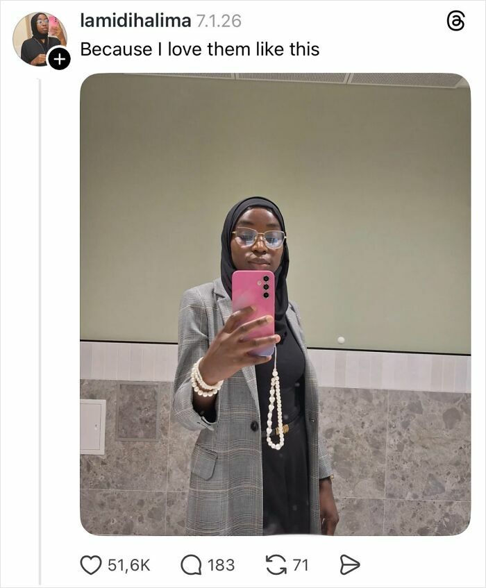 Woman taking a mirror selfie showing natural nails, wearing glasses and a hijab in a gray checked blazer.