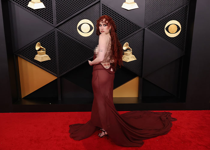 Chappell Roan in a flowing maroon gown posing on the Grammy red carpet with Grammy and CBS logos in the background. Chappell Roan in a flowing maroon gown posing on the Grammy red carpet with Grammy and CBS logos in the background.