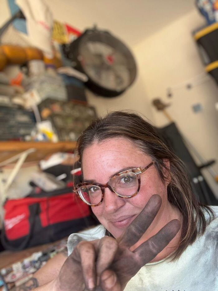 Woman with dirty hands making peace sign in a workshop, highlighting why girls don’t get their nails done discussion.