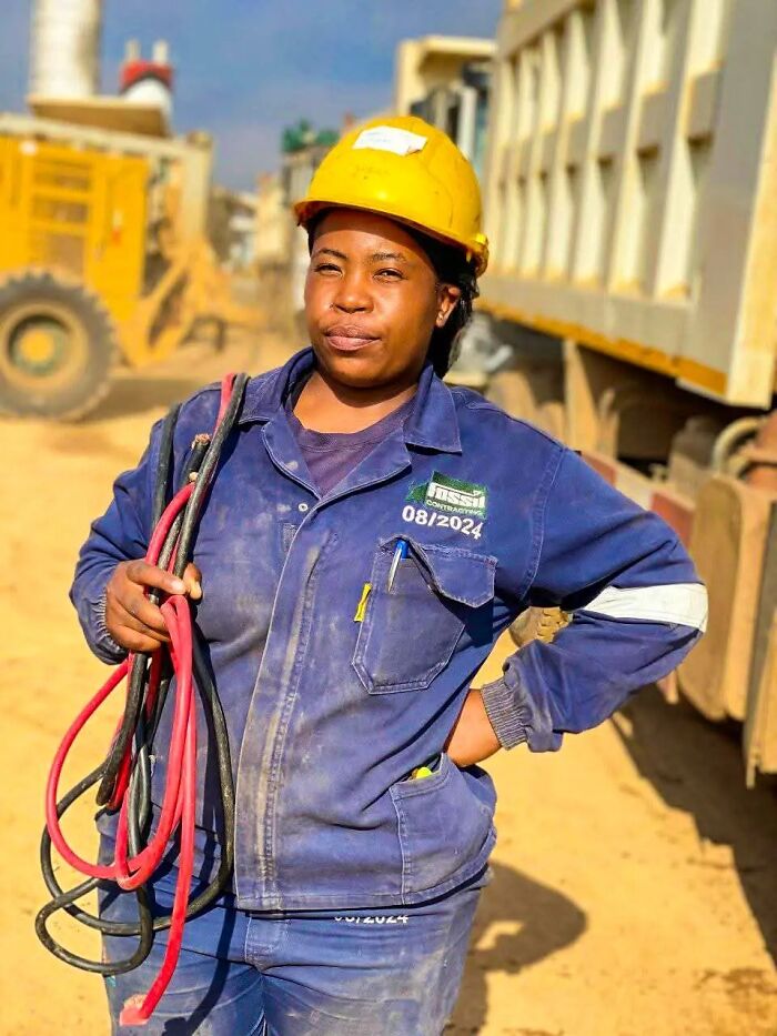 Woman construction worker wearing a yellow helmet holding cables at a worksite, showing confidence without nails done.