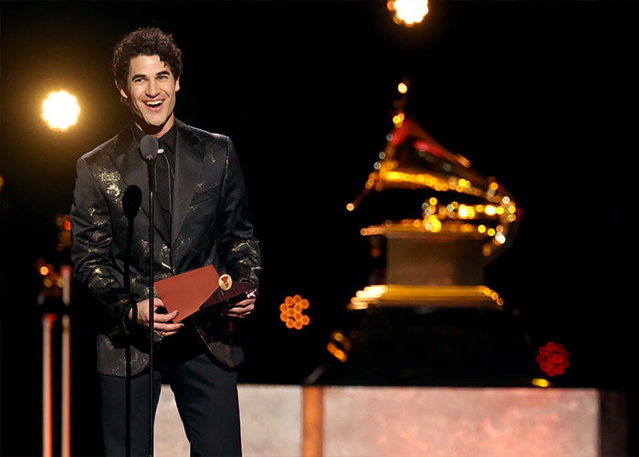 Young man in a black patterned suit holding an envelope onstage during a cringe moment at the 2026 Grammy Awards ceremony.