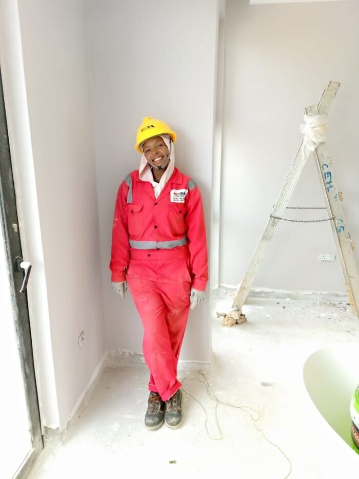 Young woman in construction gear smiling at a work site, challenging why girls don’t get their nails done.