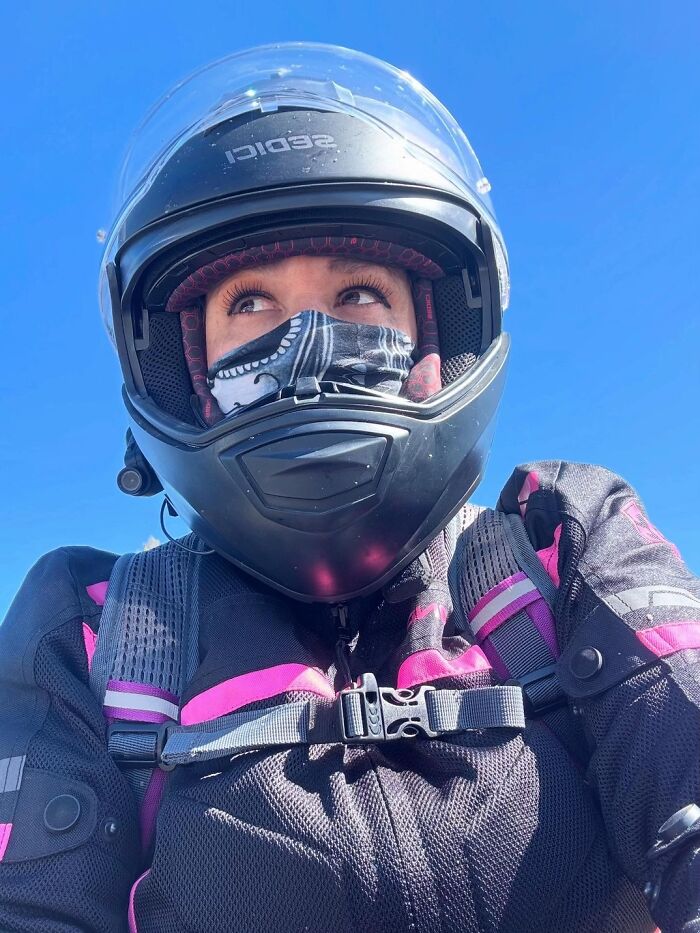 Woman wearing a motorcycle helmet and protective jacket with pink accents under clear blue sky, focusing on nails discussion topic.