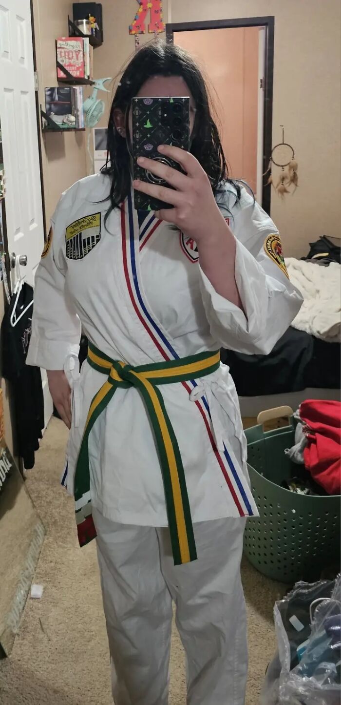 Woman in martial arts uniform taking mirror selfie showing nails without polish or manicure in bedroom setting