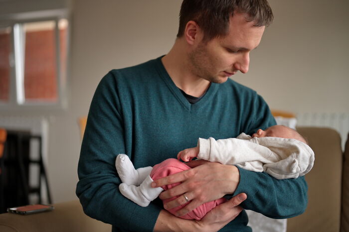 Man in teal sweater holding a sleeping baby, capturing a tender moment related to funny things said under anesthesia.