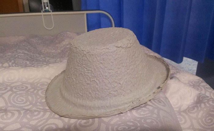 Worn hospital bed with blue curtain background and a crumpled paper hat resting on the blanket.