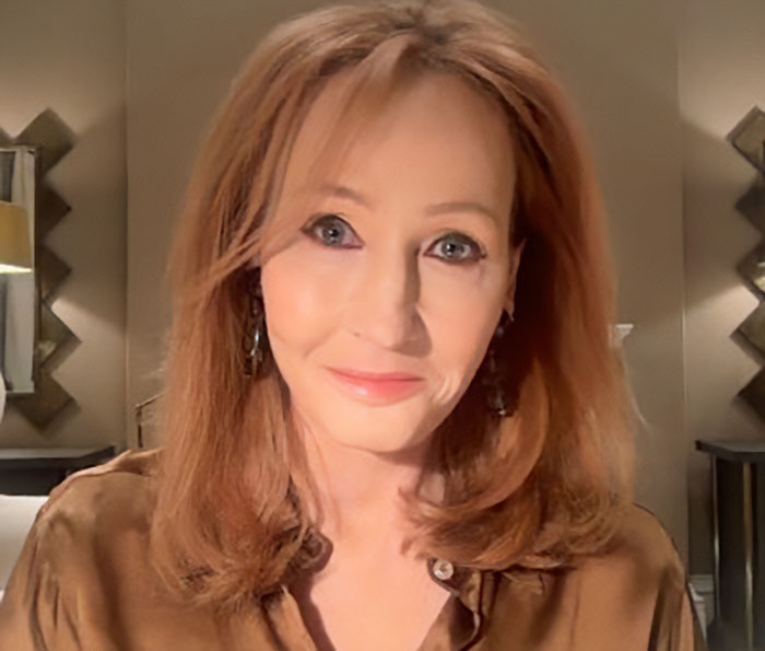 J.K. Rowling with red hair, wearing brown top and earrings, sitting indoors in a softly lit room discussing Epstein accusations. J.K. Rowling with red hair, wearing brown top and earrings, sitting indoors in a softly lit room discussing Epstein accusations.