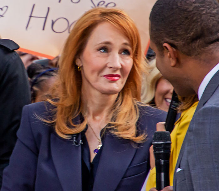 J.K. Rowling in a navy blazer speaking with a man during a public event amid Epstein accusations discussion.