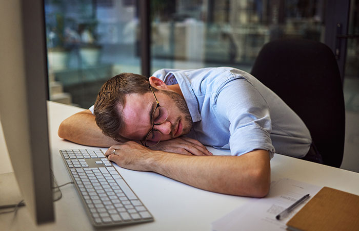 Man sleeping at his desk in an office, illustrating coworkers sharing the fastest they saw colleagues getting fired.