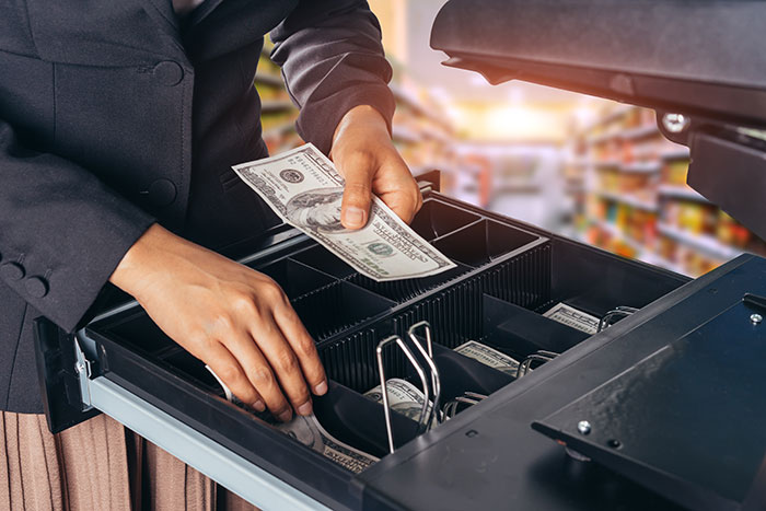 Person handling cash in a cash register drawer, illustrating a fast moment at work related to getting fired.
