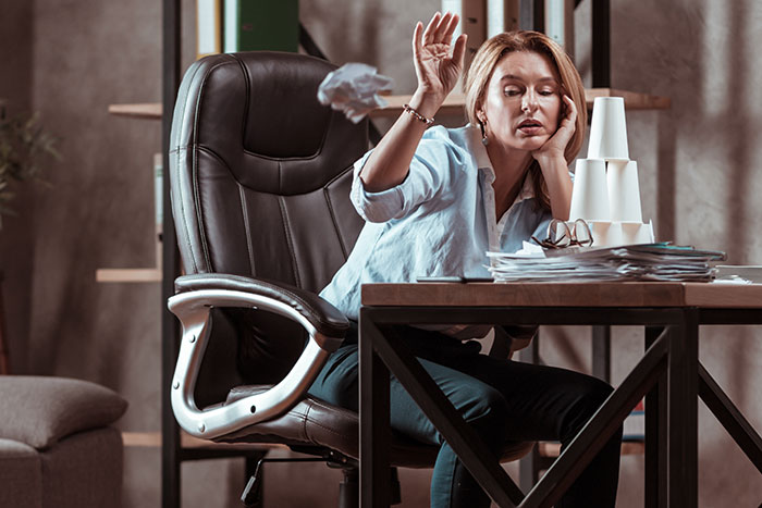 Woman at office desk looking frustrated, stacking paper cups, symbolizing fast coworker firing and desk flipping.