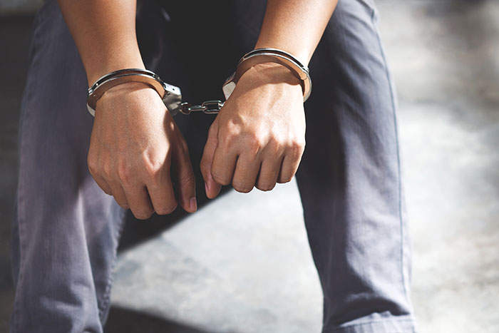Person sitting with hands cuffed in handcuffs, symbolizing consequences related to coworkers getting fired quickly.