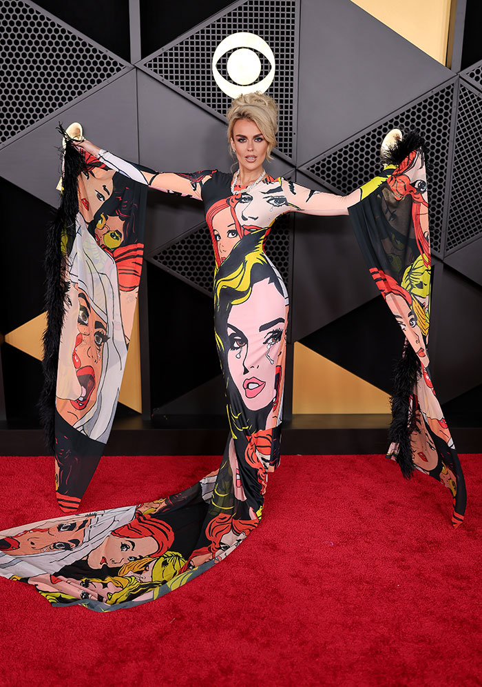 Woman posing on red carpet wearing colorful dress with dramatic sleeves featuring stylized face prints at 2026 Grammys fashion fails.