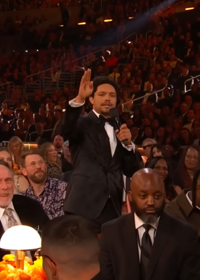 Trevor Noah in a black tuxedo speaking into a microphone at the Grammys, sparking wild theories among the audience. Trevor Noah in a black tuxedo speaking into a microphone at the Grammys, sparking wild theories among the audience.