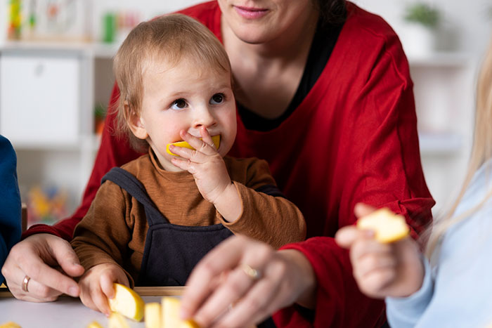 Toddler biting fruit slice with adult helping, illustrating 20 MILs that won the absolute worst in January.