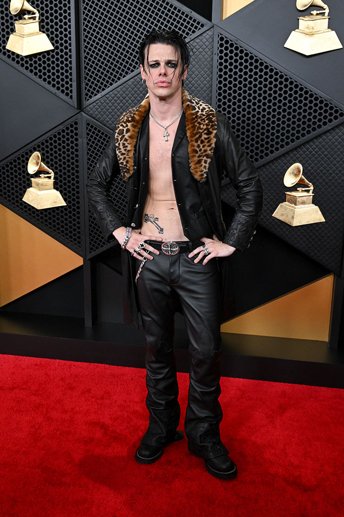 Male celebrity in leather pants and a fur-collared jacket posing on the red carpet fashion fails Grammys 2026.