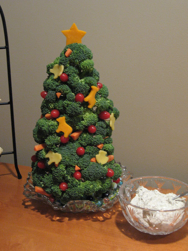 Creative DIY Christmas tree made of broccoli, cherry tomatoes, and cheese shapes, with a dip bowl beside it.