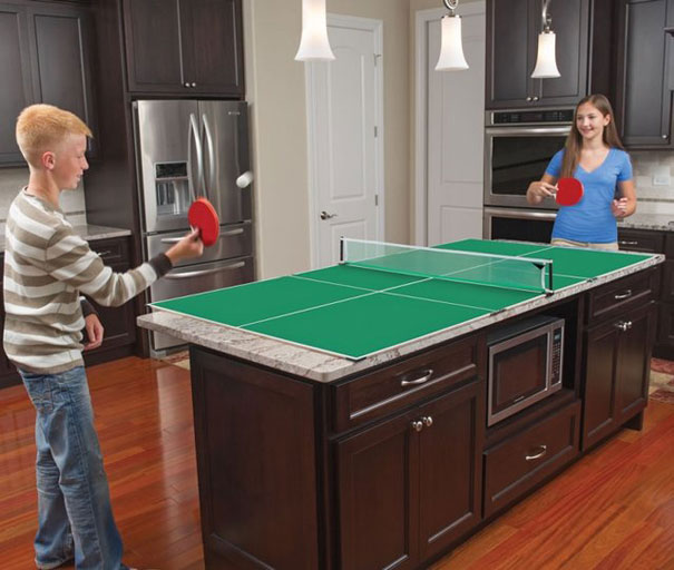 Two kids playing table tennis on a convertible ping pong kitchen island in a modern home design. Two kids playing table tennis on a convertible ping pong kitchen island in a modern home design.