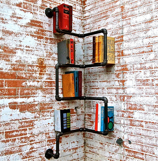 Creative bookshelf design made of black pipes against a textured brick wall, displaying various colorful books.