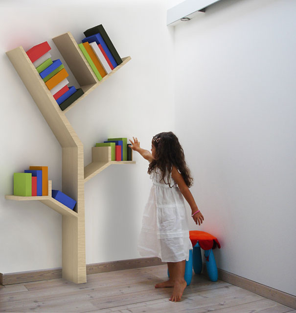 Child reaching for books on a tree-shaped bookshelf design against a white wall.