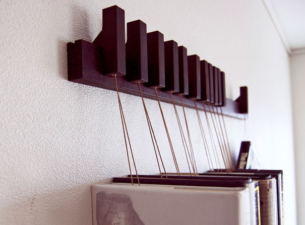 Creative bookshelf design with vertical black slats suspended on strings, holding books against a white wall.