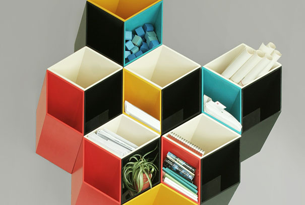 Creative bookshelf design with colorful, hexagonal compartments holding books, plants, and rolled papers.