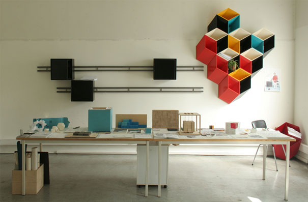 Creative bookshelf design featuring colorful geometric cubes on a wall above a desk with various objects. Creative bookshelf design featuring colorful geometric cubes on a wall above a desk with various objects.