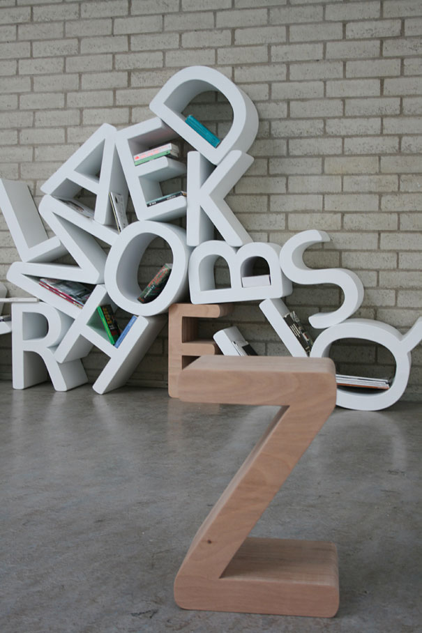 Creative bookshelf design with letters forming a unique shelving structure against a brick wall.