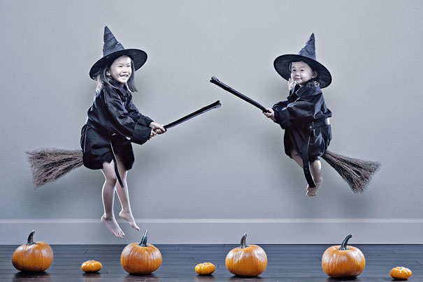 Two daughters dressed as witches flying on brooms over pumpkins in a creative dad's crazy photo shoot.