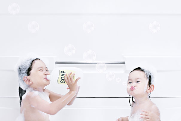 Two young daughters covered in bubbles playing with soap in a bathtub in a creative dad photo setup.