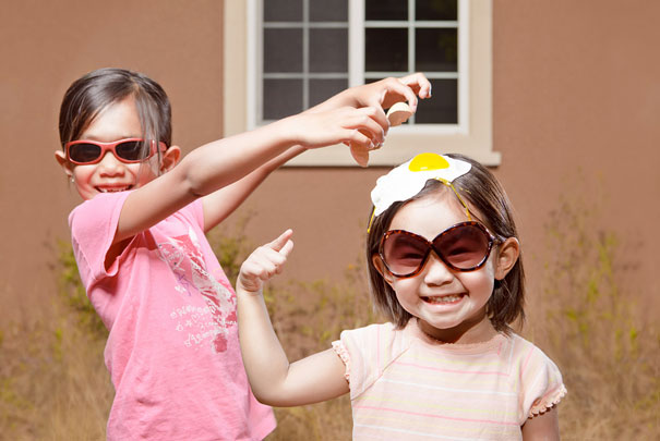 Two daughters wearing sunglasses with a creative dad capturing crazy photos of them in a playful outdoor setting