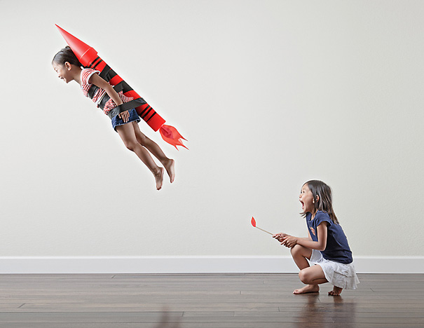 Creative dad captures fun and crazy photos of daughters playing with a rocket prop in a minimalist indoor setting.