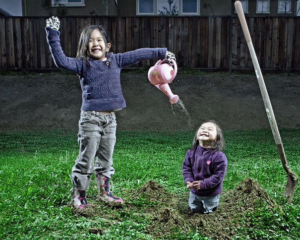 Two daughters playing outdoors with one pouring water from a pink watering can, showcasing creative dad's crazy photo idea.