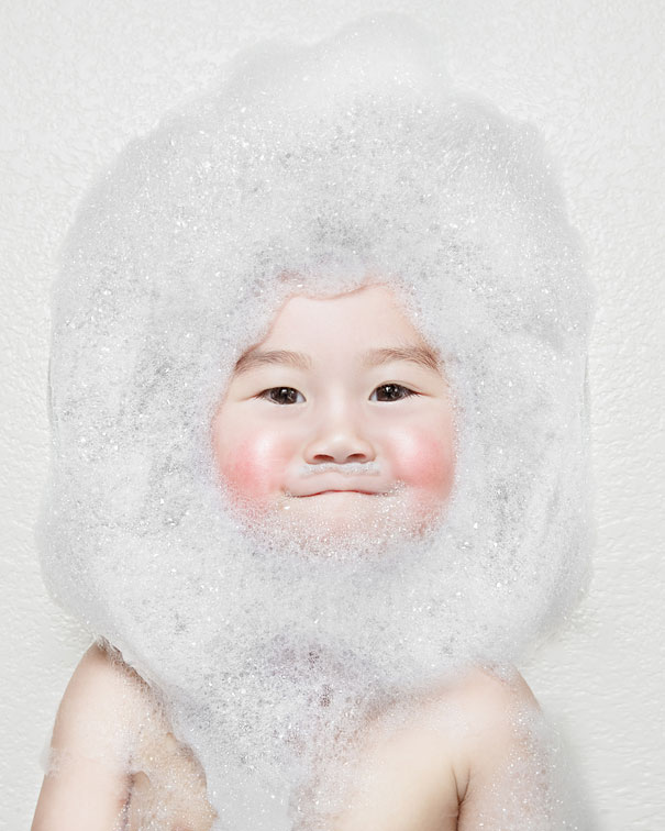 Creative dad takes crazy photos of daughter covered in bubbles with playful expression against white background