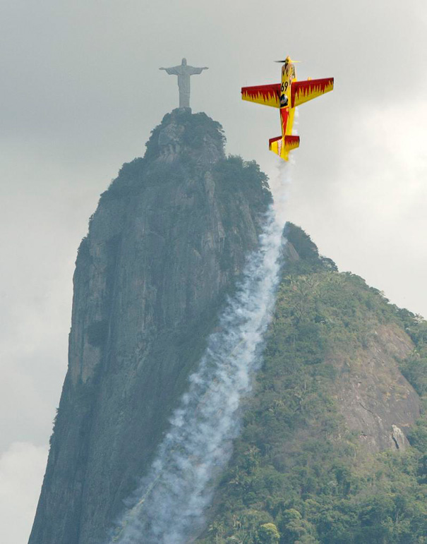A perfectly timed photo of an airplane flying near Christ the Redeemer statue, trailing smoke against a cloudy sky. A perfectly timed photo of an airplane flying near Christ the Redeemer statue, trailing smoke against a cloudy sky.