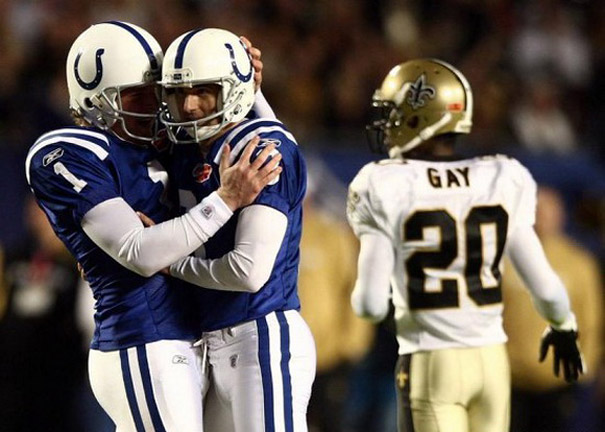 Football players in blue jerseys hug, with a player in white walking by, showcasing a perfectly timed photo moment. Football players in blue jerseys hug, with a player in white walking by, showcasing a perfectly timed photo moment.
