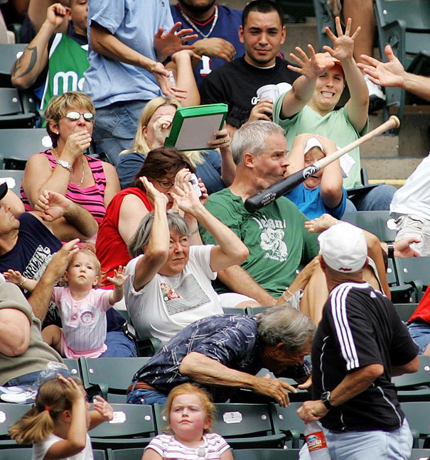 Crowd at a baseball game reacting as a bat flies into the stands, a perfectly timed photo capturing the moment.