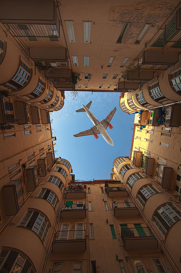 Perfectly timed photo of a plane flying above a narrow courtyard with tall buildings on a sunny day. Perfectly timed photo of a plane flying above a narrow courtyard with tall buildings on a sunny day.
