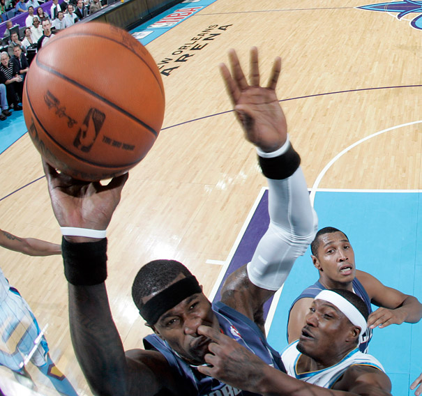 Basketball game with perfectly timed photo of a player shooting the ball, defenders jumping to block in a crowded arena.