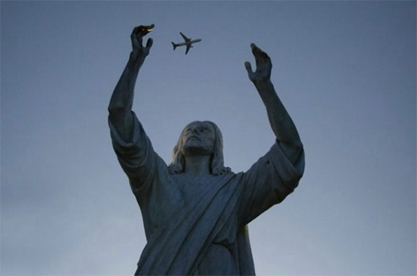 Statue reaching towards a perfectly timed airplane, creating an illusion of holding it in the sky.