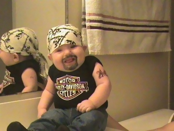 Baby dressed in Harley-Davidson biker costume with bandana, black shirt, and fake tattoo for kids' Halloween costume.